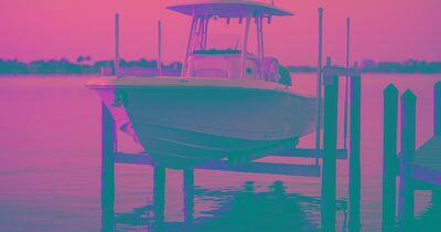 A center-console boat resting on a four-post aluminum elevator lift above calm Sarasota Bay at golden hour