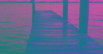 A weathered wooden dock extending over calm Sarasota Bay at golden hour with a pelican perched on a piling