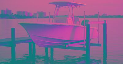 A white center-console boat resting on a four-post boat lift above calm Sarasota Bay at golden hour
