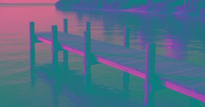 A wooden dock extending over calm Sarasota Bay at golden hour, warm sunlight reflecting off the water
