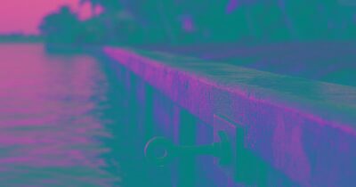 Weathered concrete seawall along a Sarasota bay waterfront at golden hour, with a steel tie-rod connection visible on the wall face