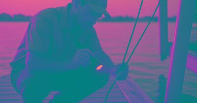 Marine technician inspecting a boat lift cable on a wooden dock at golden hour over calm Sarasota Bay