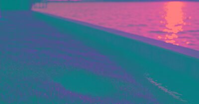 A soft depression in a Florida waterfront yard near a concrete seawall at golden hour, suggesting soil loss behind the wall